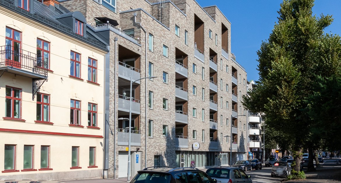 Rad av bostadshus längs Kungsgatan. Till vänster ett äldre gulmålat hus med röda fönster, och intill ett modernt hus i ljus tegel med flera balkonger.