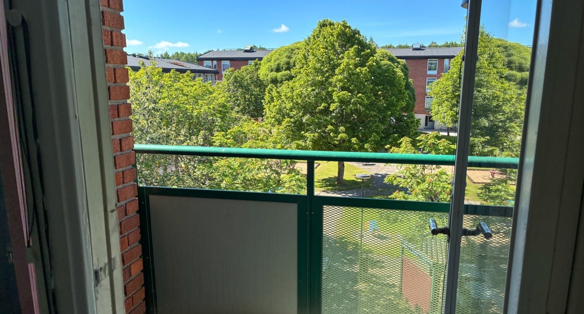 Utsikt från balkongen mot en grön innergård med träd och gräsytor.