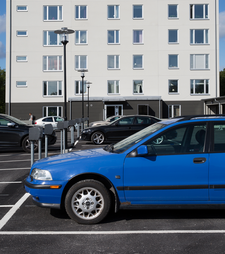 Blå bil står parkerad framför ett höghus.