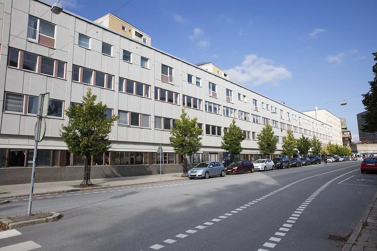 Exteriör med fastighet på Drottninggatan 46 med många fönster och bilparkering längs gatan utanför.