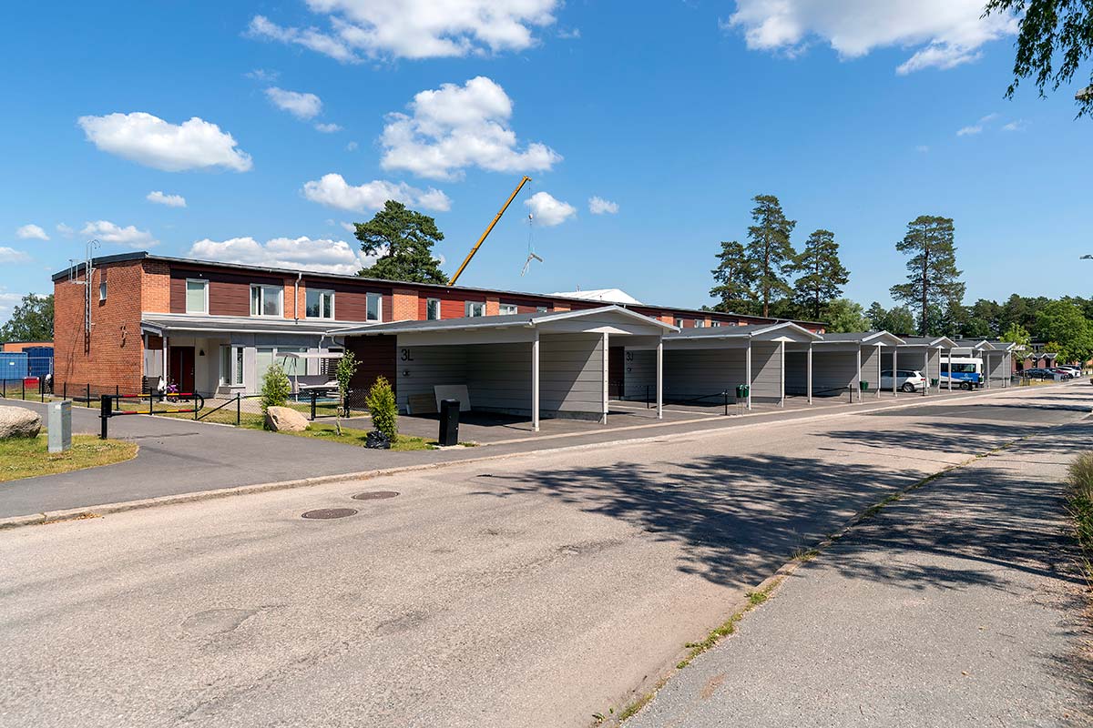 Tegelhus i två våningar med carport framför och en lyftkran i bakgrunden