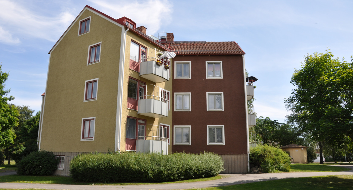 Hus i tre våningar med gul och brun fasad och vita balkonger.