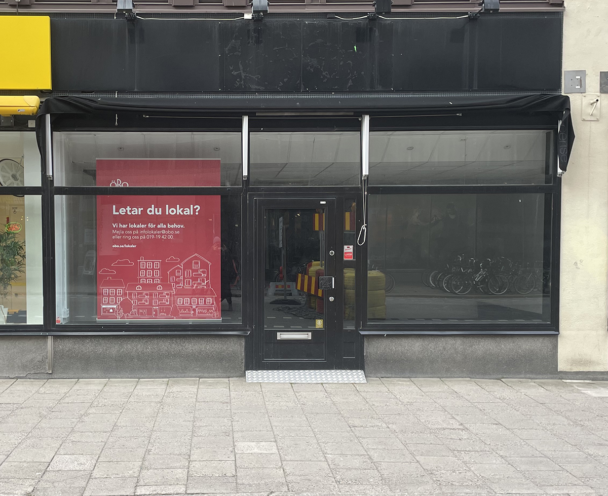 Entré till lokal i gatuplan på Drottninggatan 38. Stora skyltfönster och dörr i glas.