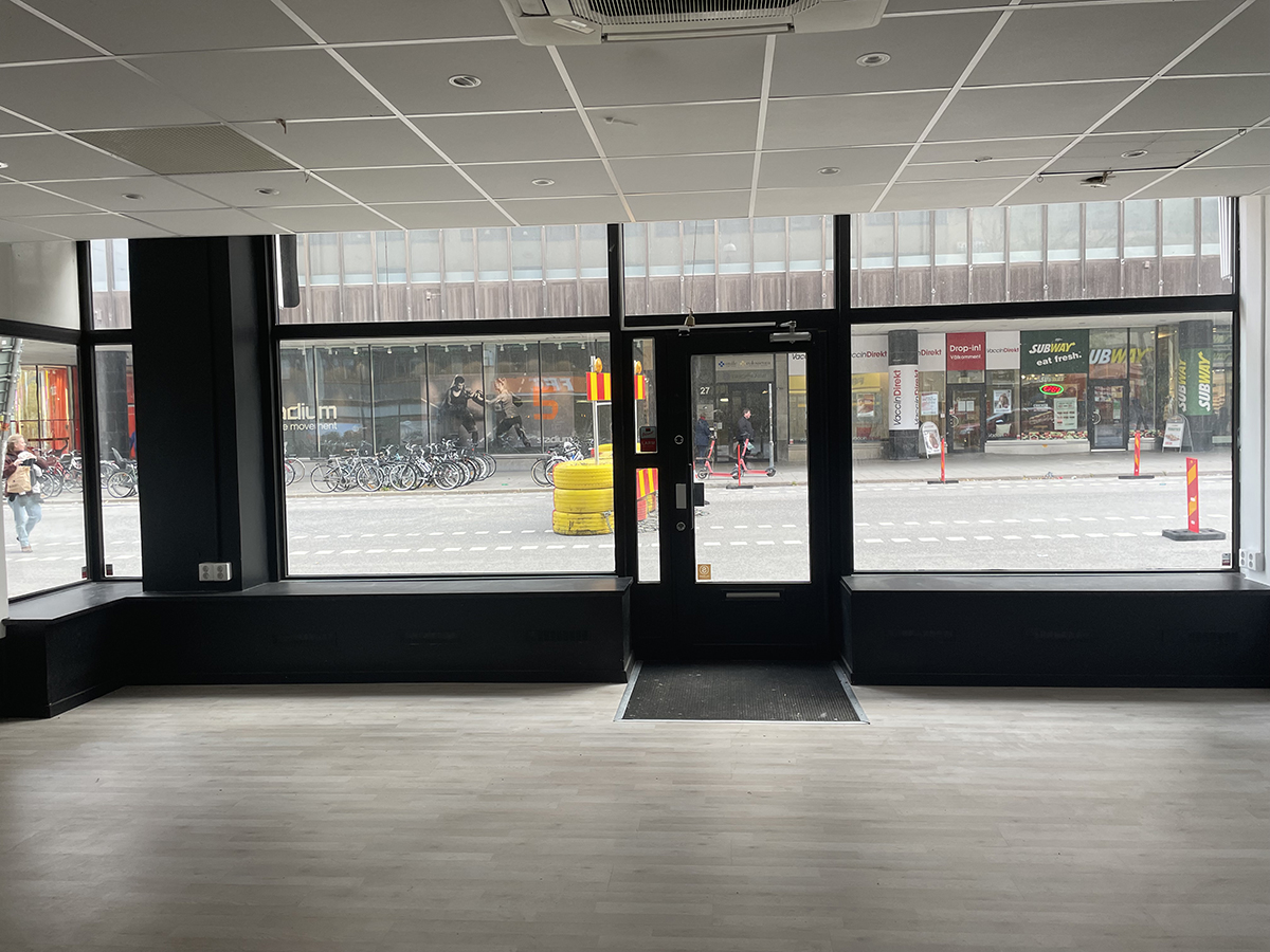 Skyltfönster och entrédörr ut mot Drottninggatan med Krämaren mittemot.