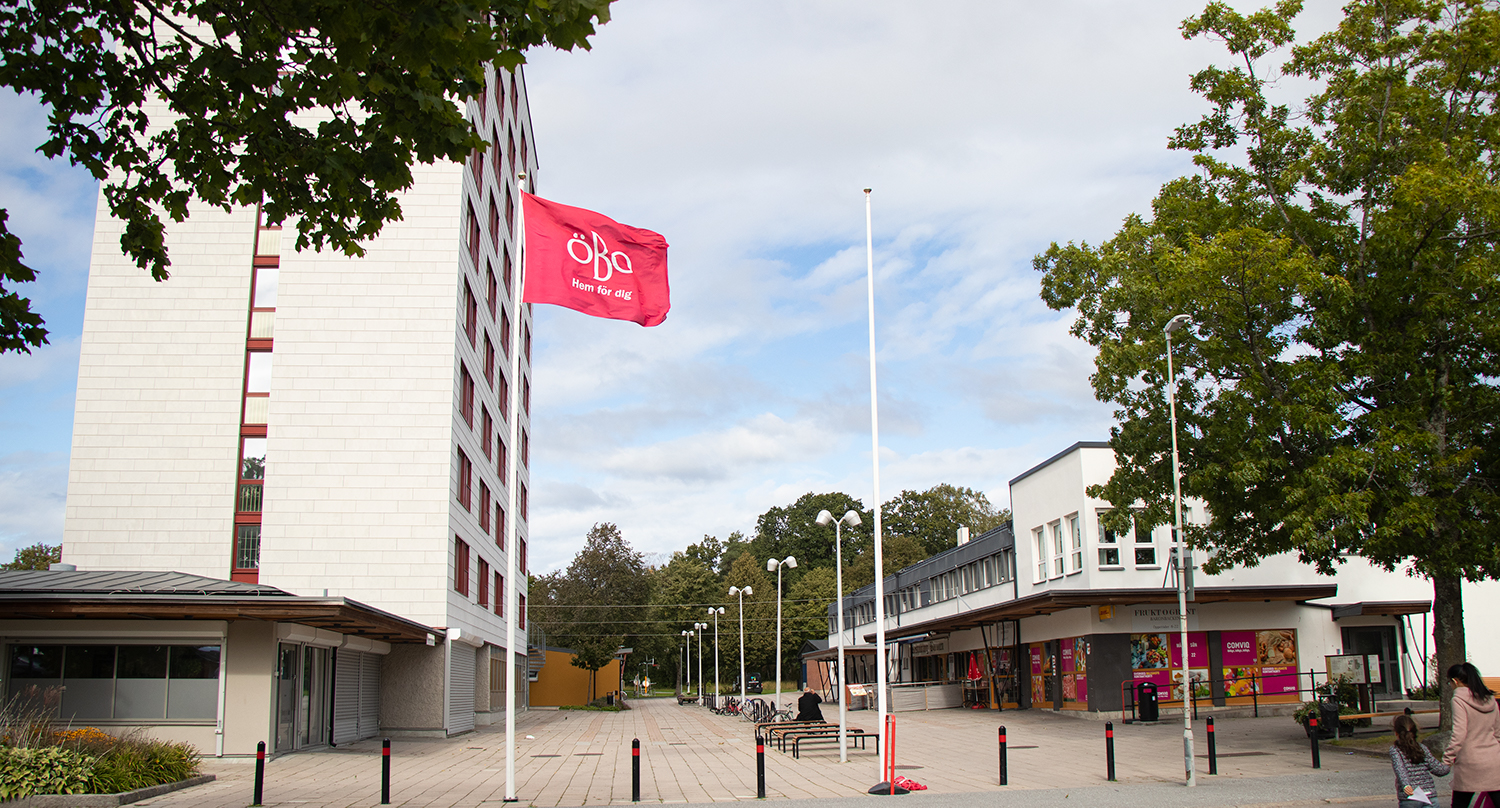 Baronbackarnas centrum med höghus och tvåvåningshus samt en flaggstång med en röd flagga med ÖBOs logotyp i vitt.