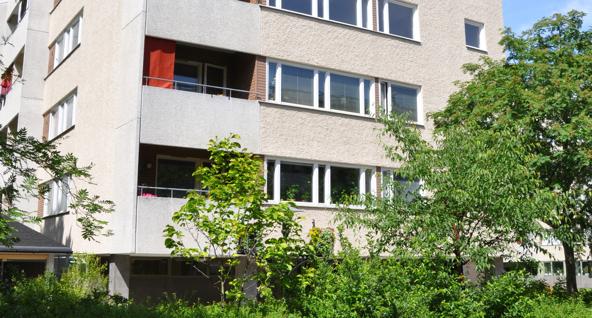 Flervåningshus med balkonger och grönskande träd utanför.