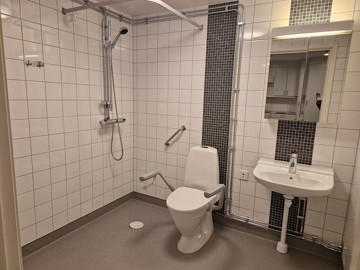 Tillgänglighetsanpassad wc med kaklade väggar, dusch, toalett och handfat