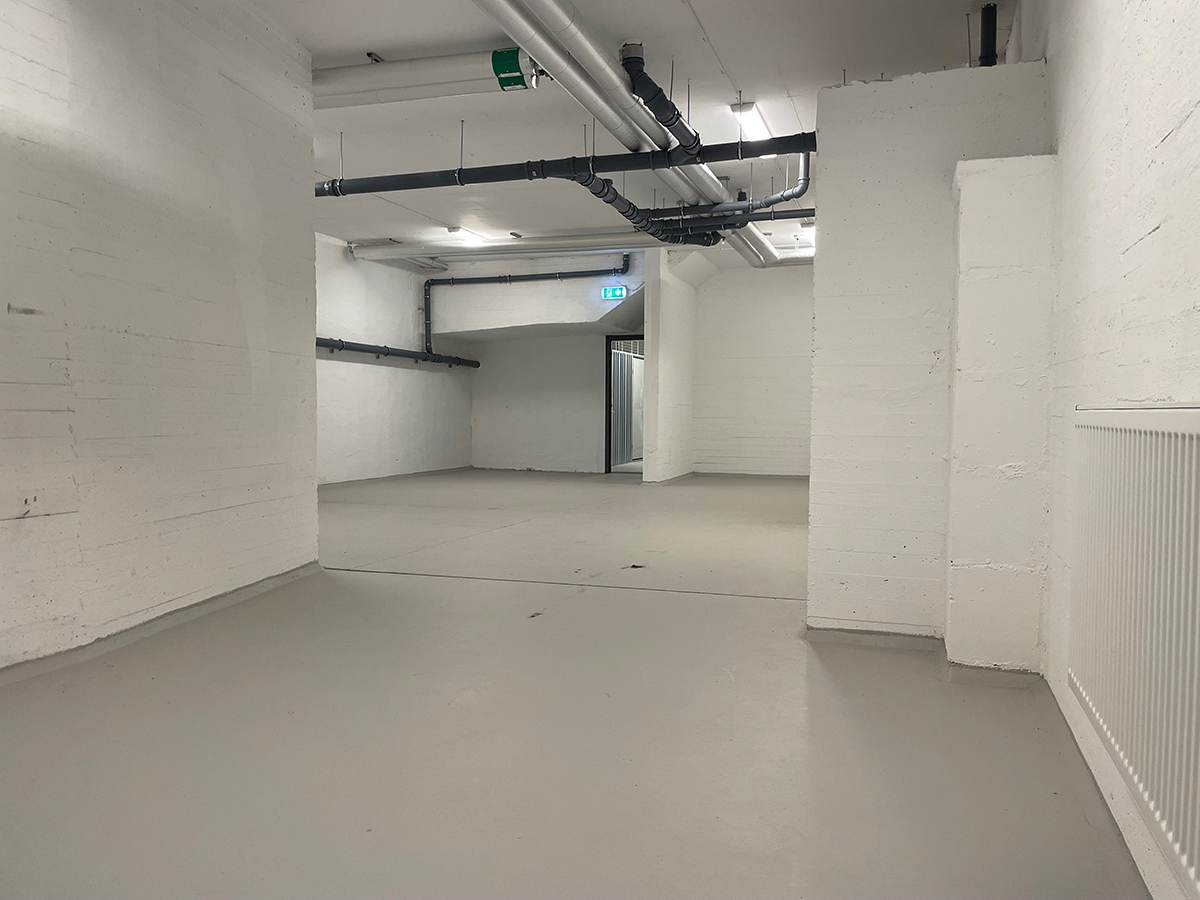 Stor lagerlokal med vitmåladeväggar och betonggolv. Takbelysning och inga fönster.