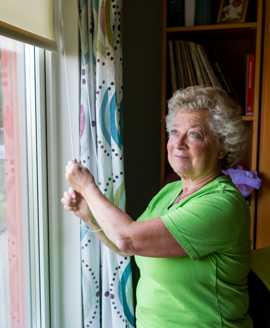 Äldre kvinna drar ner persienn. Foto: Mikael Wallerstedt för Folkhälsomyndigheten