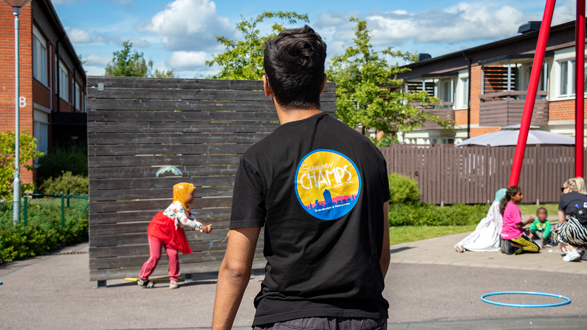 Feriepraktikant kastar frisbee med barn på en lekplats i Vivalla.