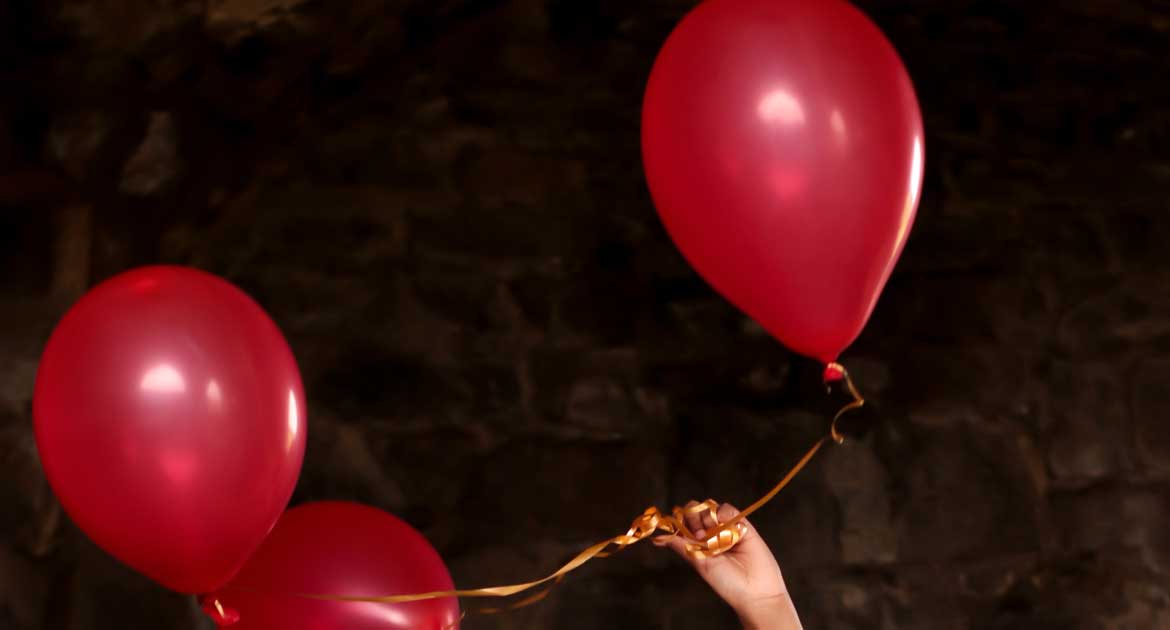 Tre röda ballonger med en guldigt snöre och en hand som håller fast dem.