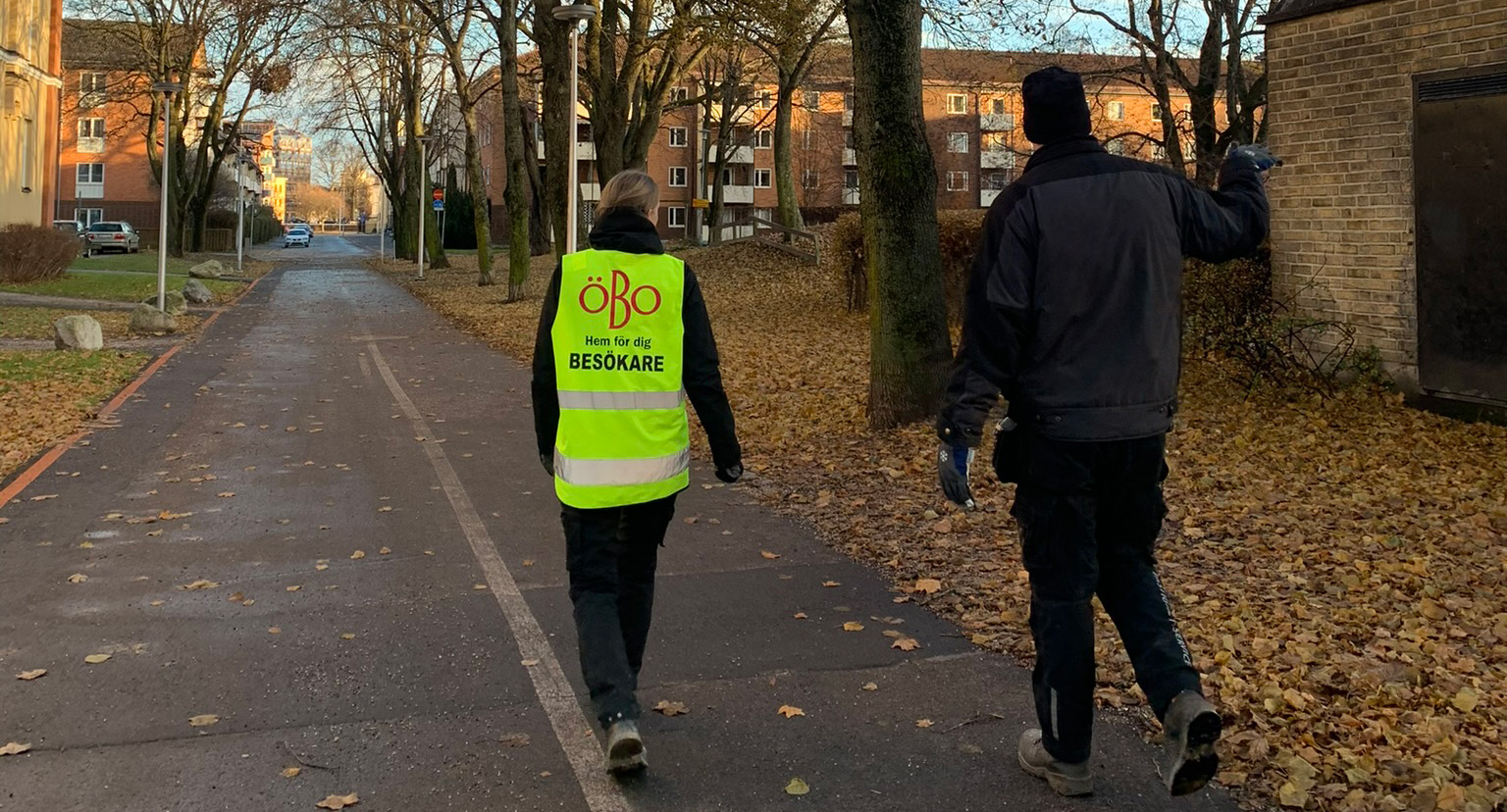 Två medarbetare från ÖBO går längs en gång- och cykelväg. På marken finns mycket fallna löv.