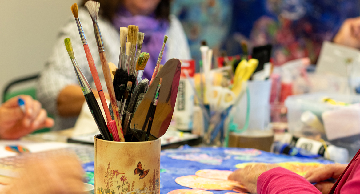 Ett färgrikt målarrum i seniorbostäder i Hjärsta. Fokus på penslar och färg på bordet.
