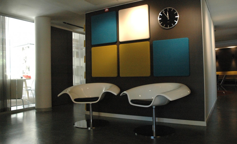 Två stolar i vit plast framför en vägg med ljuddämpande kvadrater i olika färger.