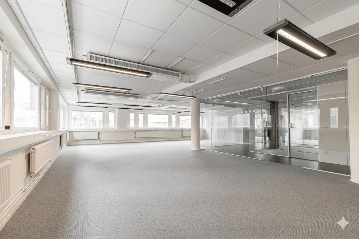 Stort öppet kontorslandskap med grå matta, många fönster längs ena väggen och glasade mötesrum.