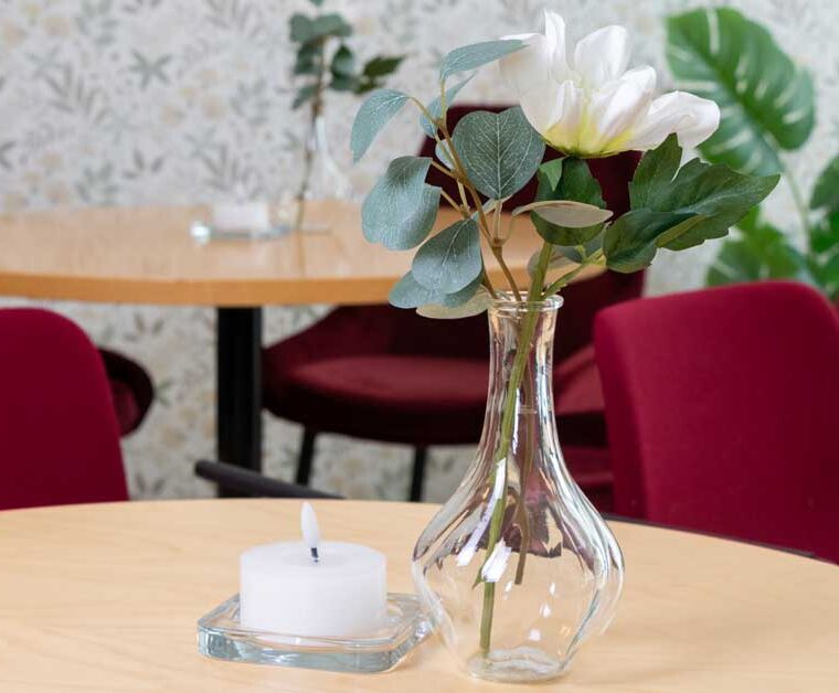 En vas med blommor och ett ljus på ett bord.