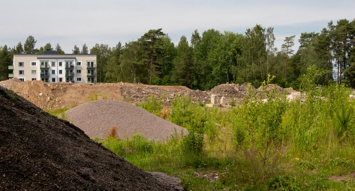 Stora grushögar samt ett hus och skog i bakgrunden.
