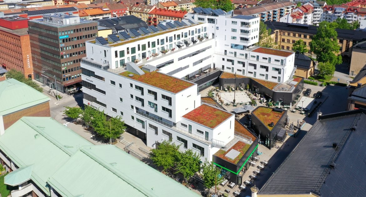 Flygbild över den vita byggnaden i kvarteret Husaren i Örebro med dess gröna tak, terrasser och restauranger runt innergården.