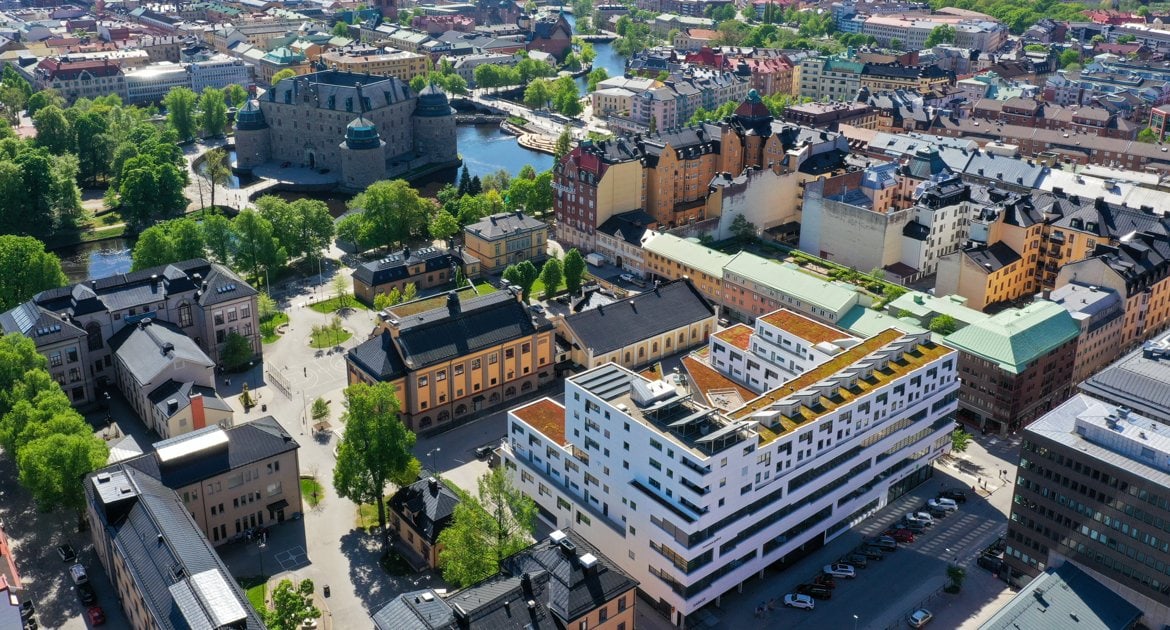 Flygbild över centrala Örebro med Örebro slott omgivet av vatten och grönska, samt den vita byggnaden i kvarteret Husaren i förgrunden.