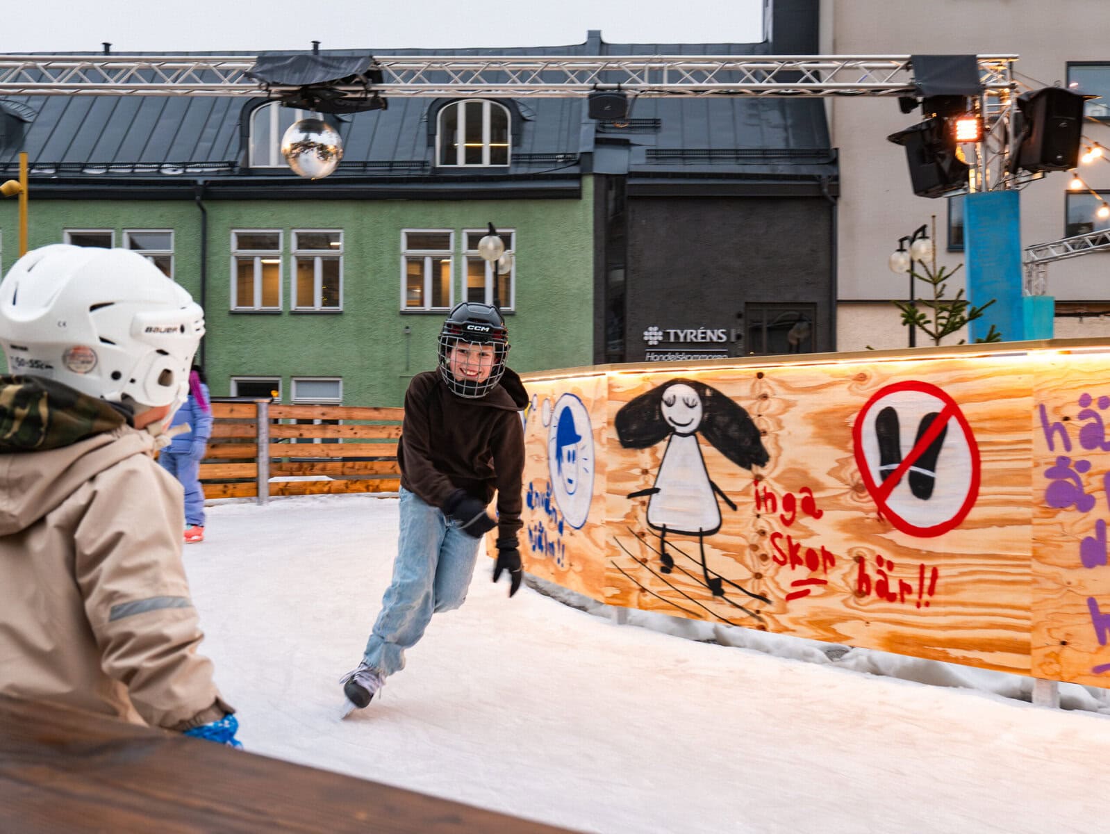 En pojke med gallerhjälm, svart tröja och jeans, åker skridskor på skridskobanan på Krämartorget.