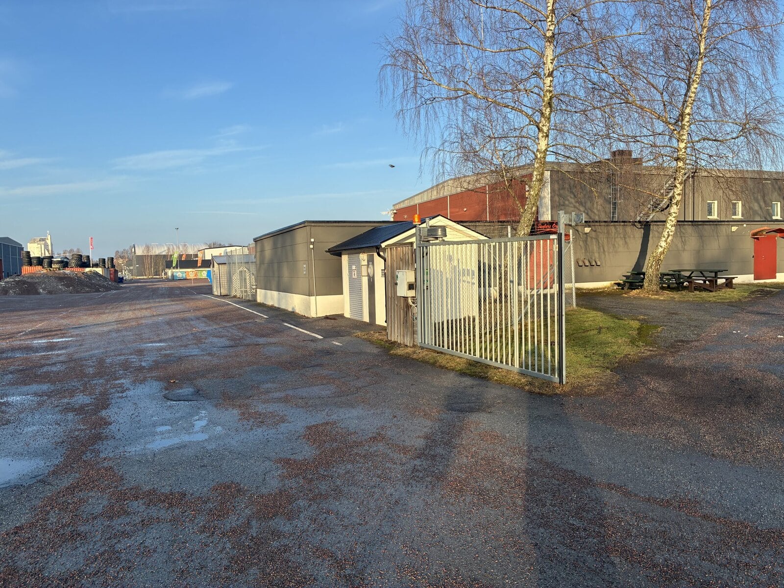 Industrifastighet med inhägnad gård och grind, asfalterad uppställningsyta samt mindre byggnad vid infarten.