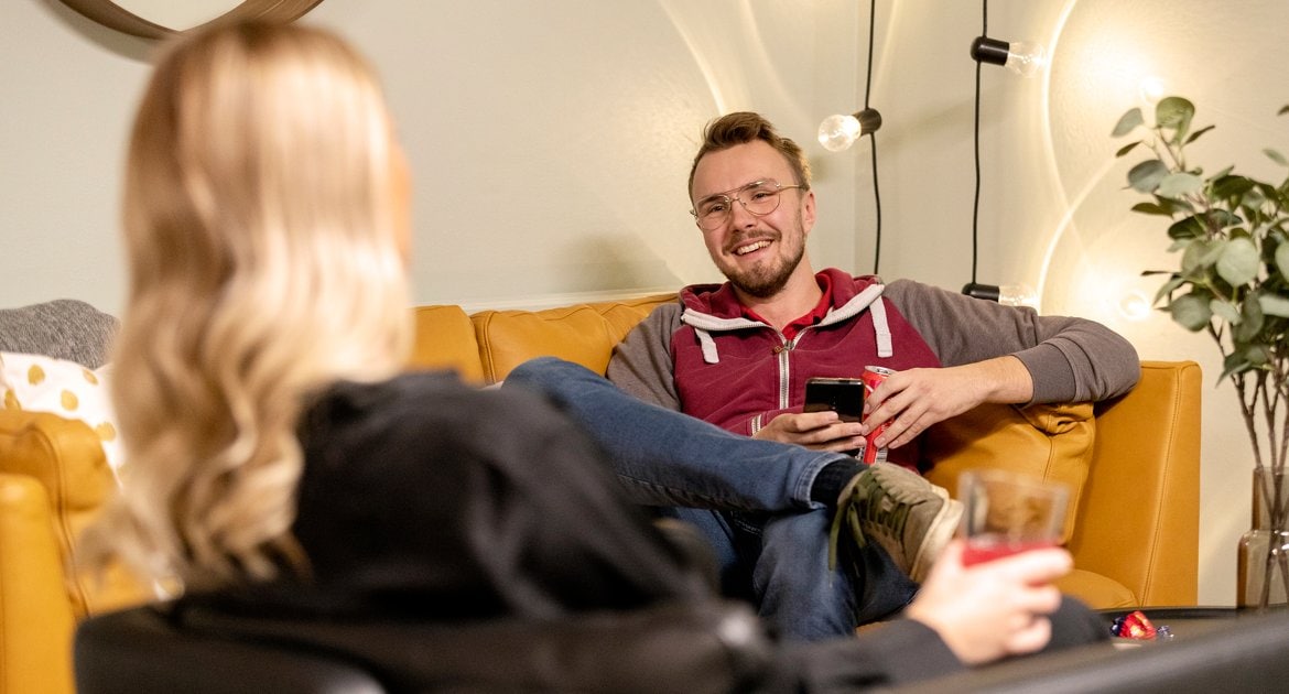 Par som sitter mitte mot varandra i i en gul soffa.
