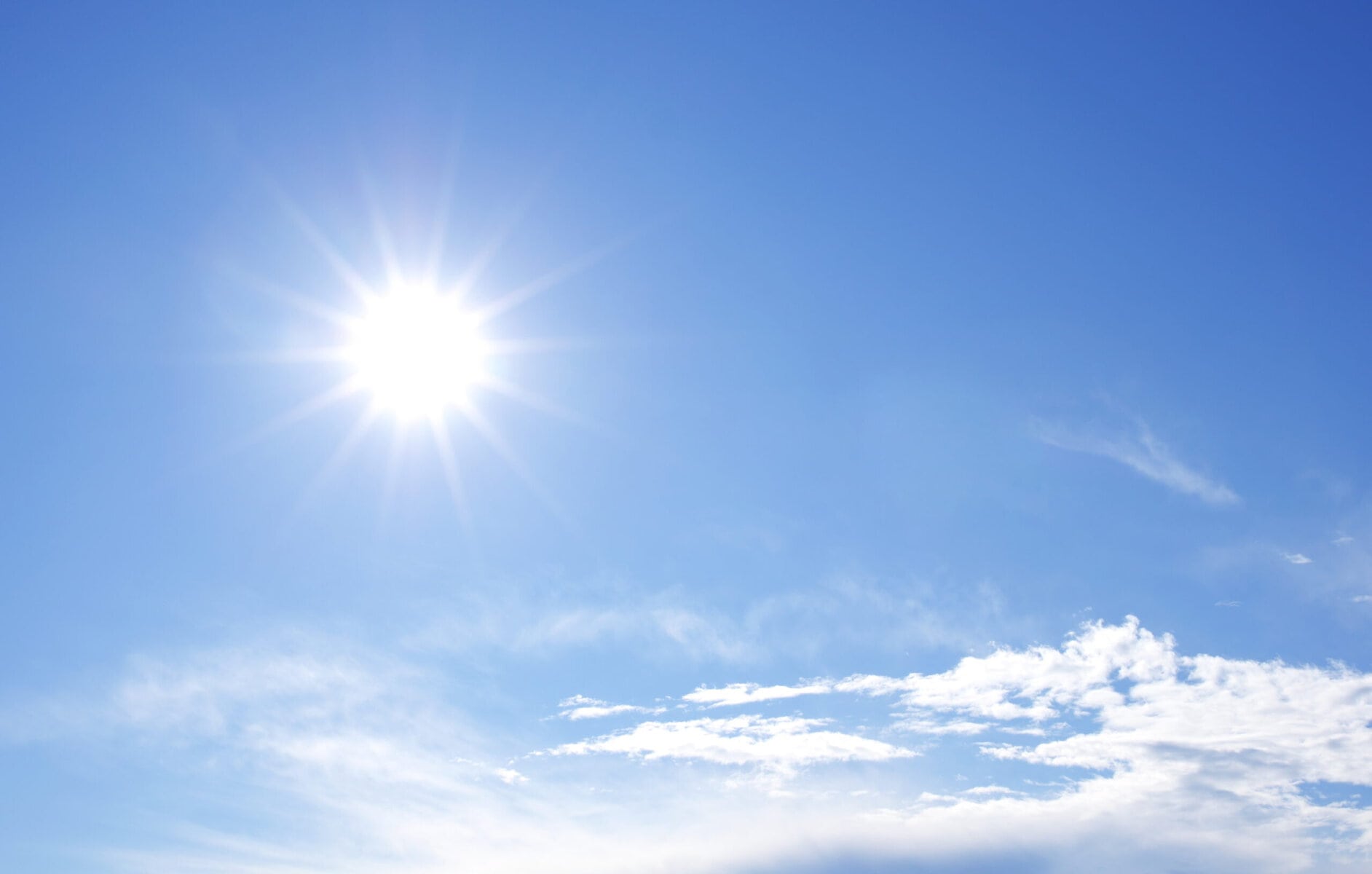 Blå himmel med strålande sol och några små moln.