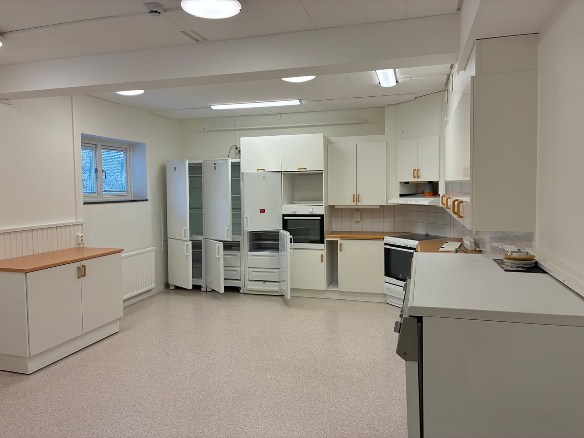 Stort kök med vita skåp, flera kylskåp, spisar och arbetsbänkar.