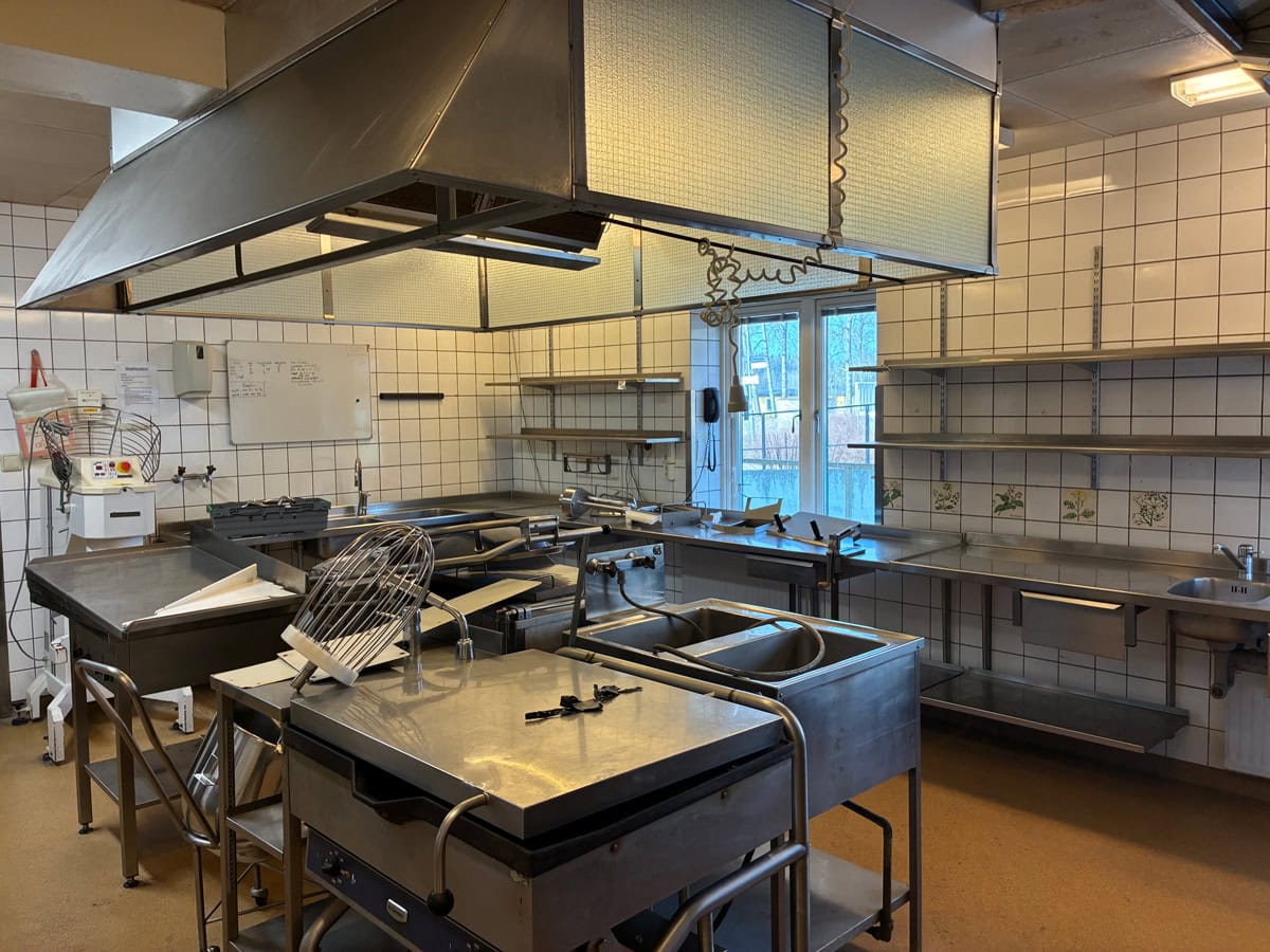 Storkök med rostfria arbetsbänkar, köksutrustning, diskhoar och stor ventilationskåpa.